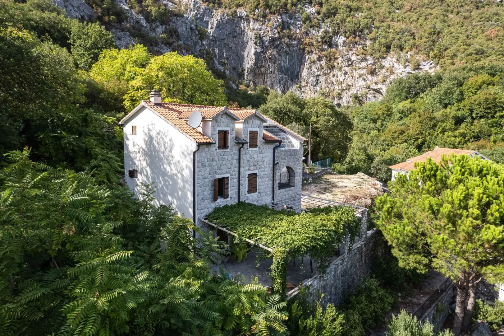 Pogled iz vazduha na kamenu kuću okruženu zelenilom i stenama.
