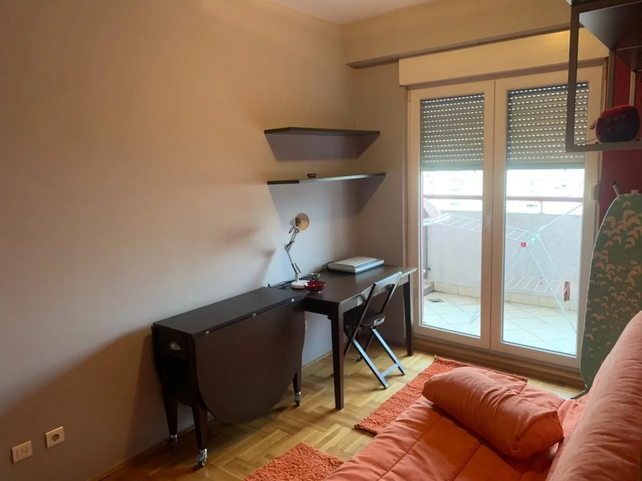 Soba sa radnim stolom, ležajem i izlazom na balkon.