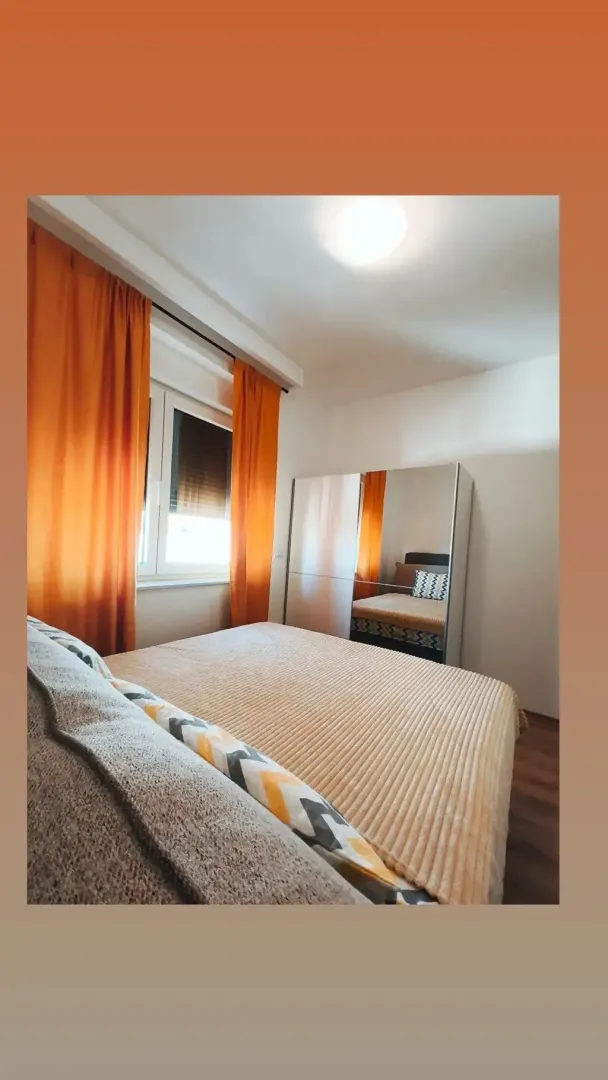 Namještena spavaća soba sa bračnim krevetom i garderoberom sa ogledalom.