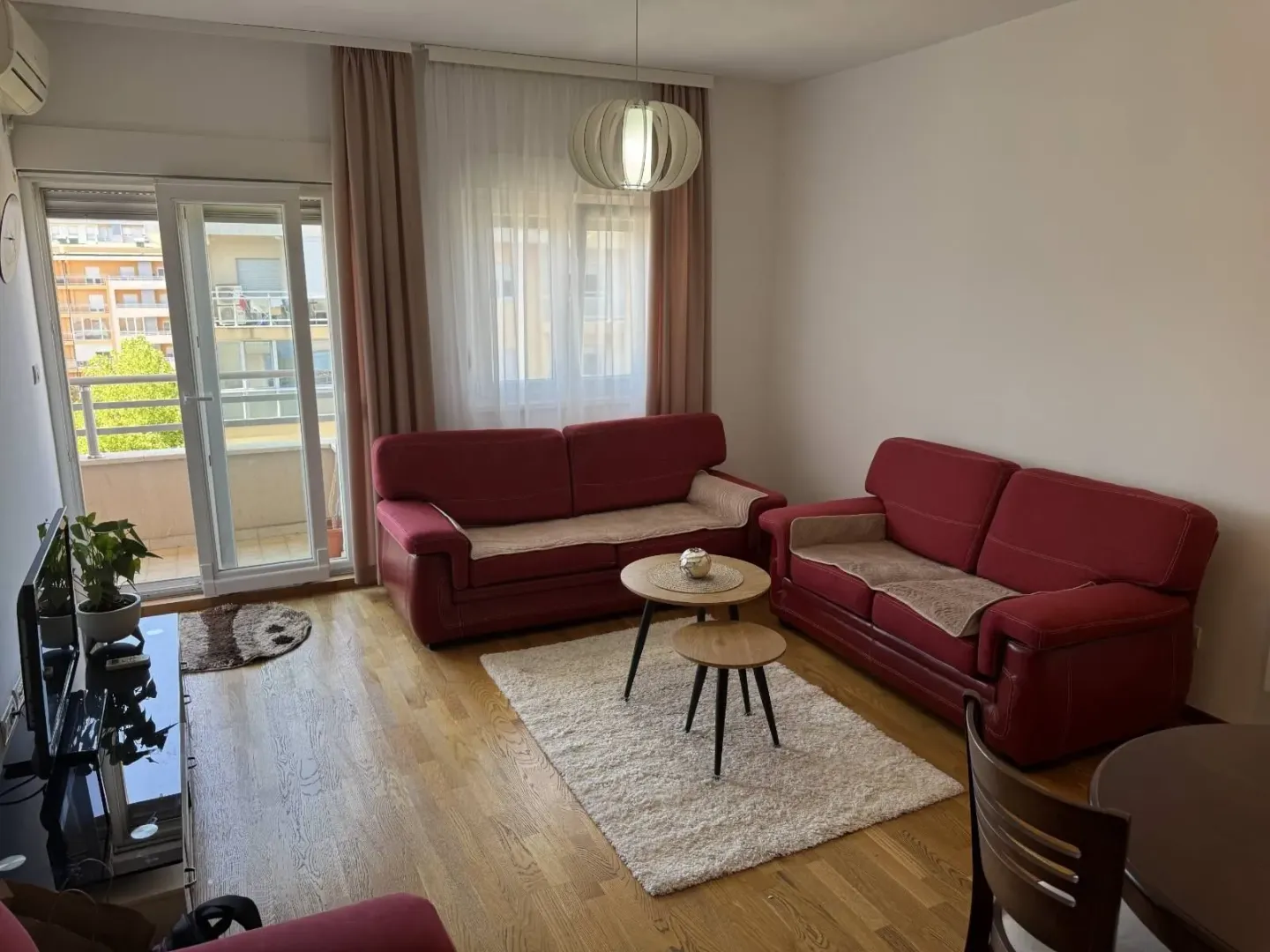 Svijetla dnevna soba sa crvenim kaučevima i izlazom na balkon.