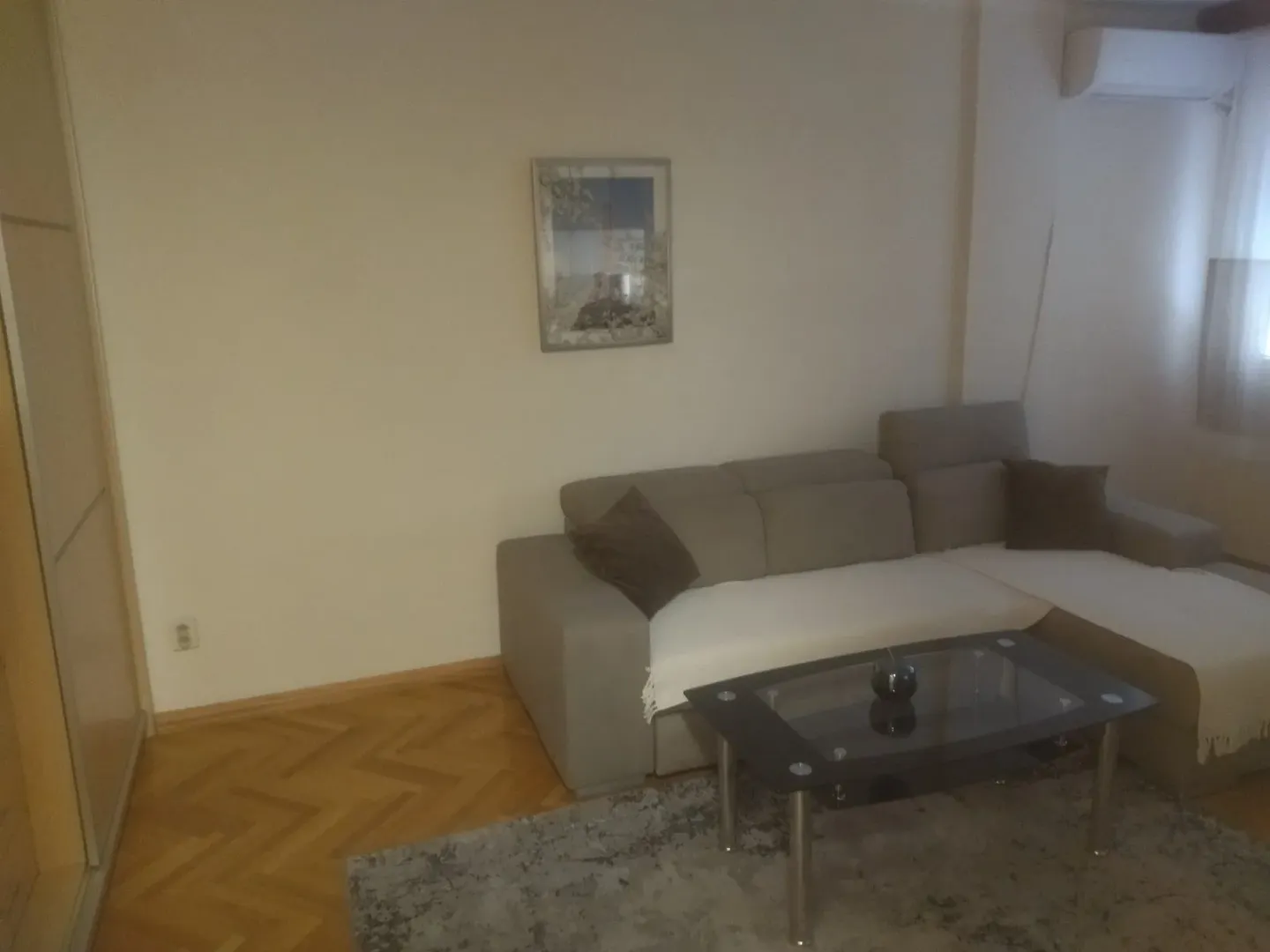 Dnevna soba sa ugaonom garniturom, stočićem i parketom na podu.