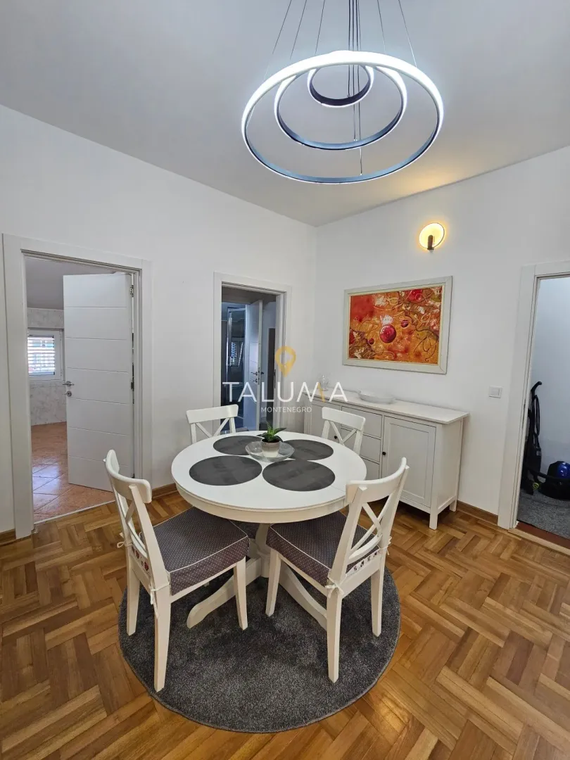 Trpezarija sa okruglim stolom, bijelim stolicama i modernim lusterom.