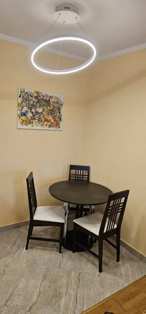 Mali trpezarijski sto sa tri stolice i modernim lusterom.