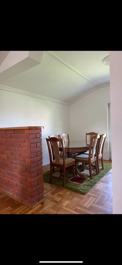 Dining area with a wooden table and chairs, parquet flooring, and a decorative brick wall.