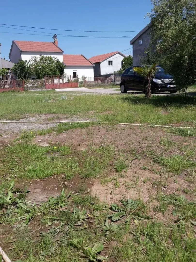 Dvorište sa travnjakom i kućama u pozadini pod vedrim nebom.