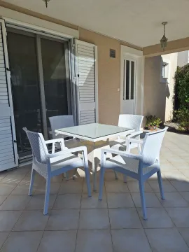 Natkrivena terasa sa trpezarijskim stolom i bijelim stolicama ispred ulaza u apartman. - image 2