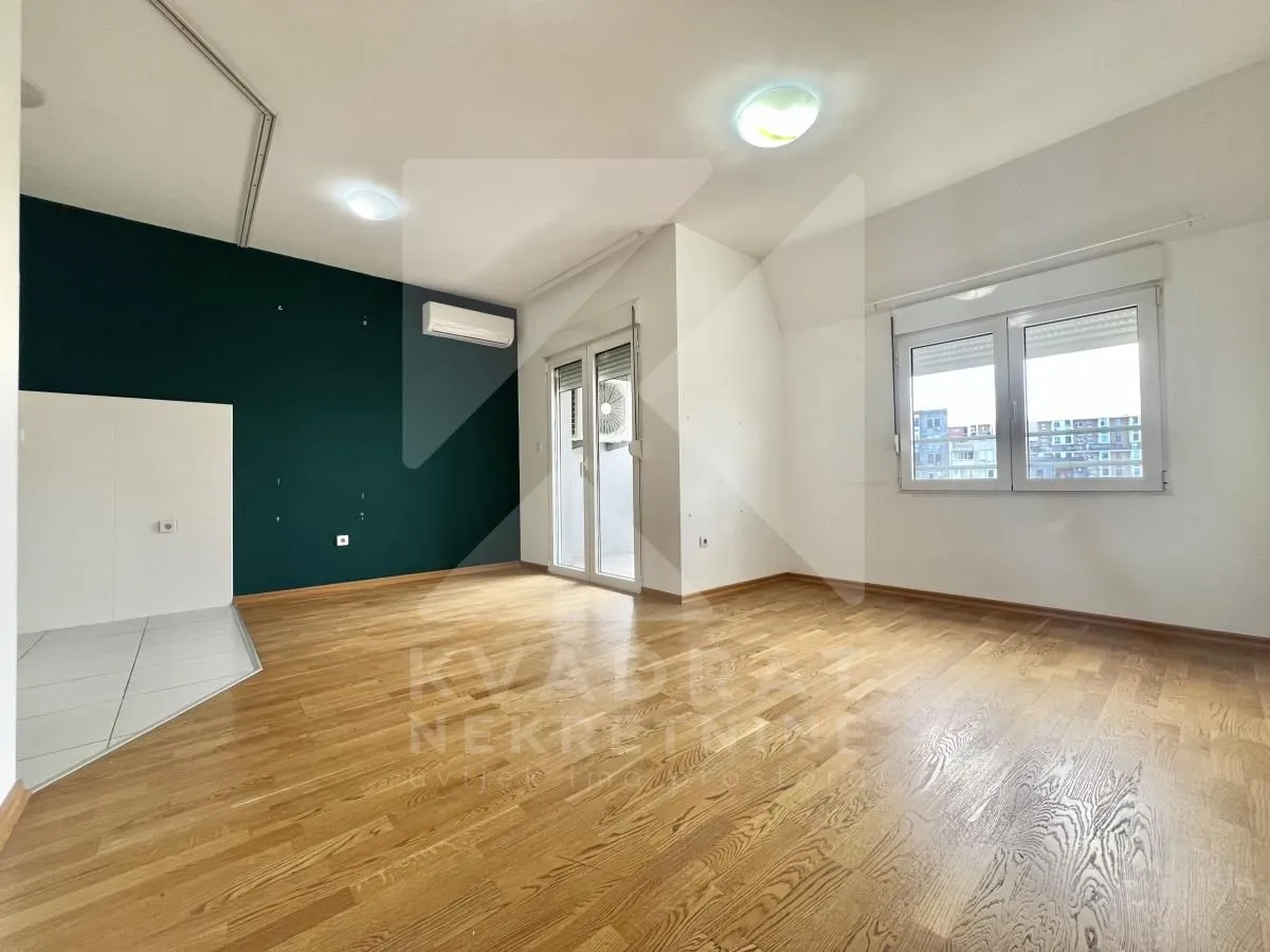 Empty living room with wooden flooring, large windows and a dark green accent wall.