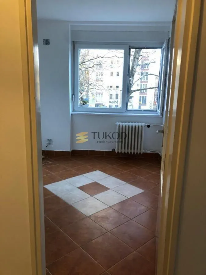 Prazna prostorija sa popločanim podom i prozorom, gledano kroz vrata.