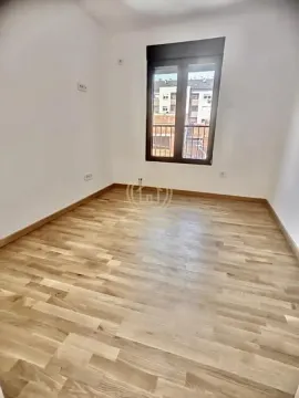 Prazna soba sa parketom i prozorom koji gleda na susedne zgrade. - image 3