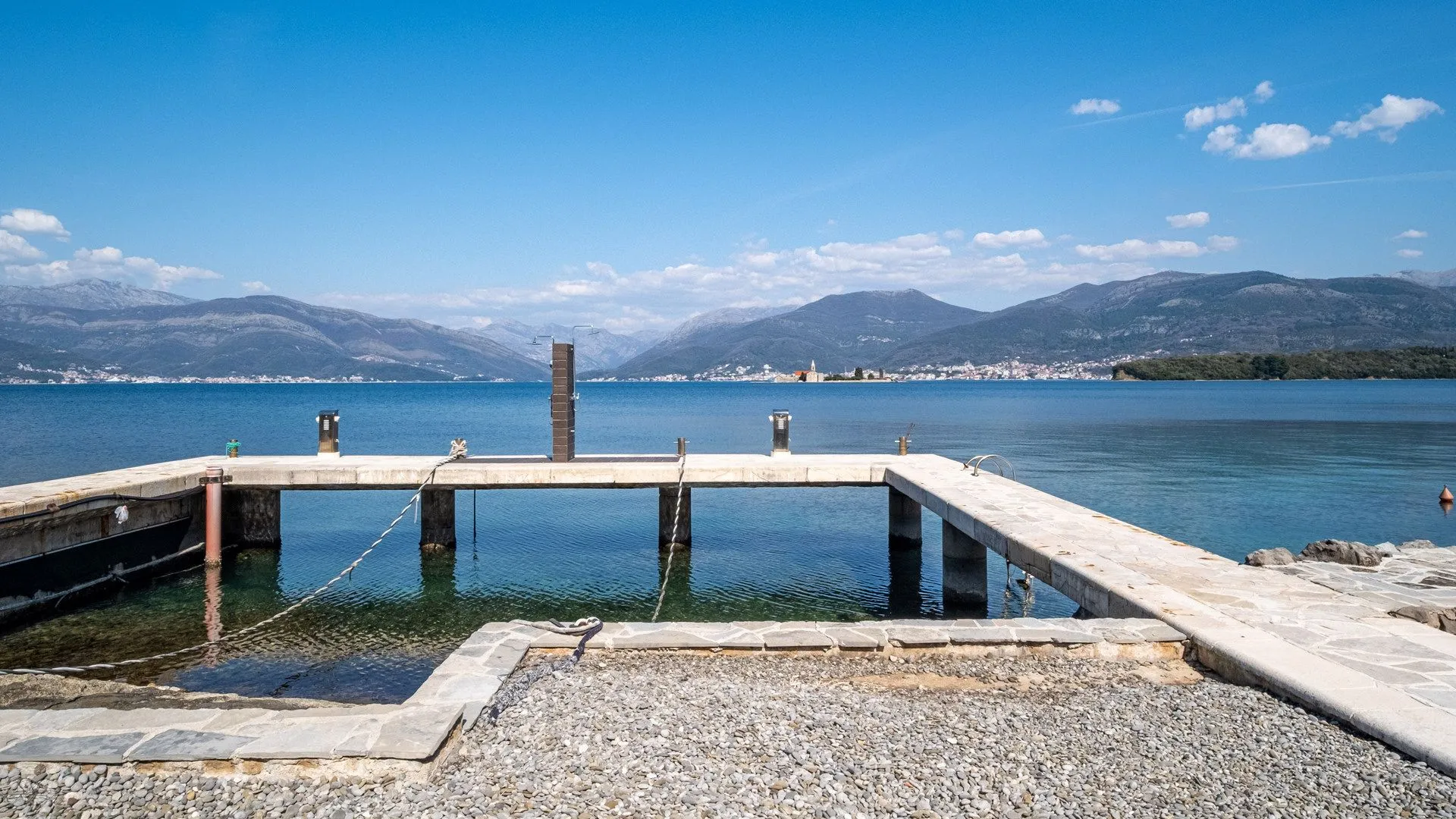 Betonska riva i mol sa pogledom na more i planine.