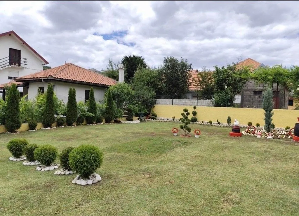 Lijepo uređeno dvorište sa travnjakom, ukrasnim rastinjem i pogledom na kuću.