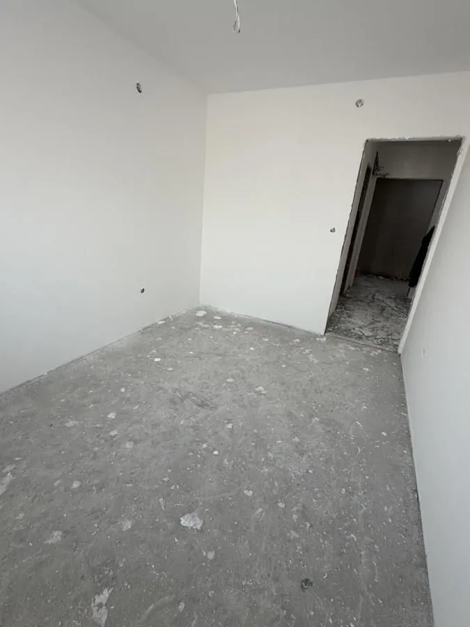 Prazna prostorija u toku građevinskih radova sa bijelim zidovima i vratima koja vode u hodnik.