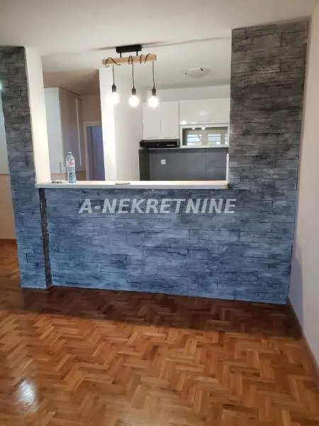 Dnevni boravak sa pogledom na kuhinju kroz šank obložen dekorativnim kamenom.