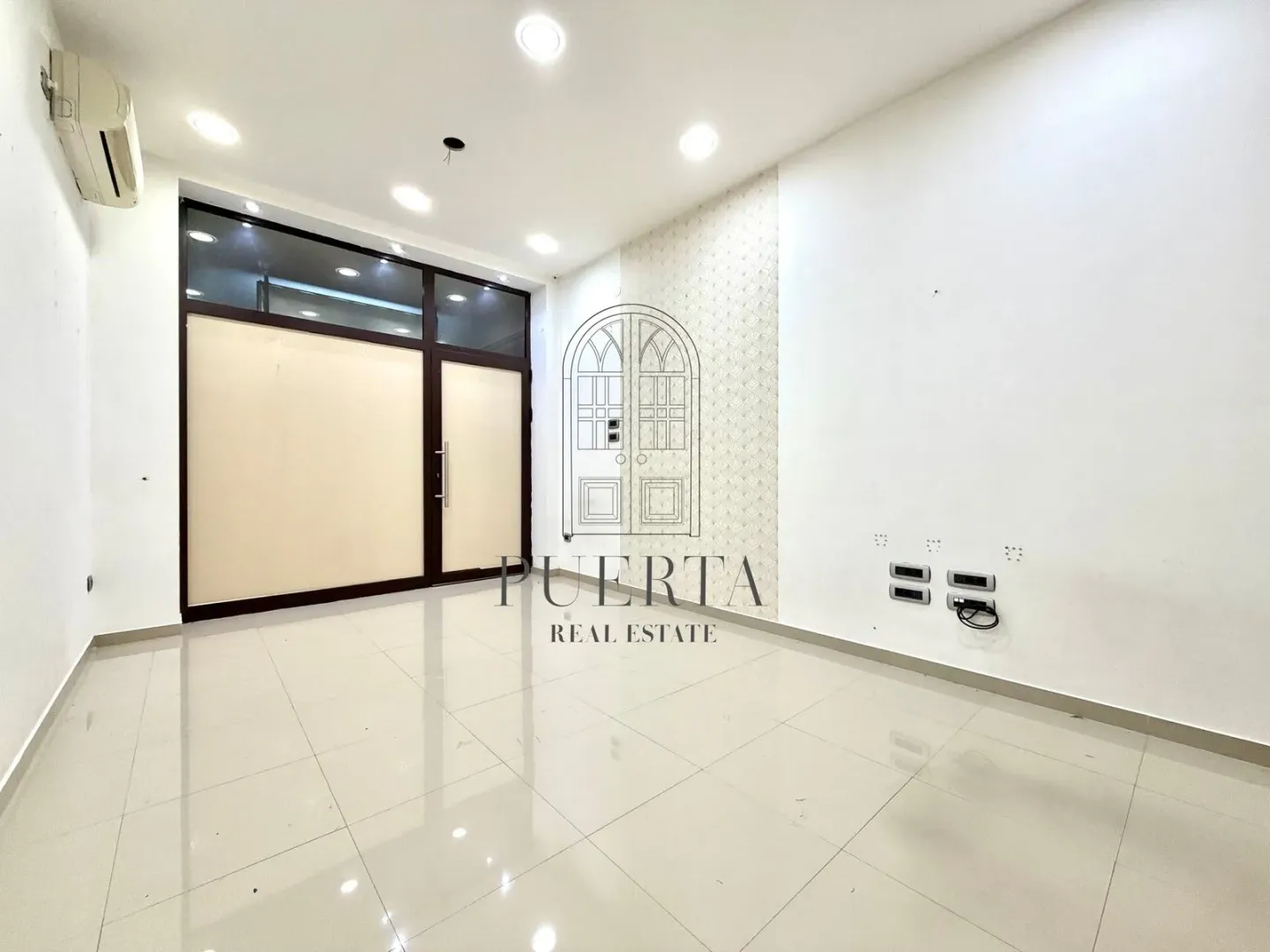 Empty bright room with tiled flooring and large glass entrance doors.