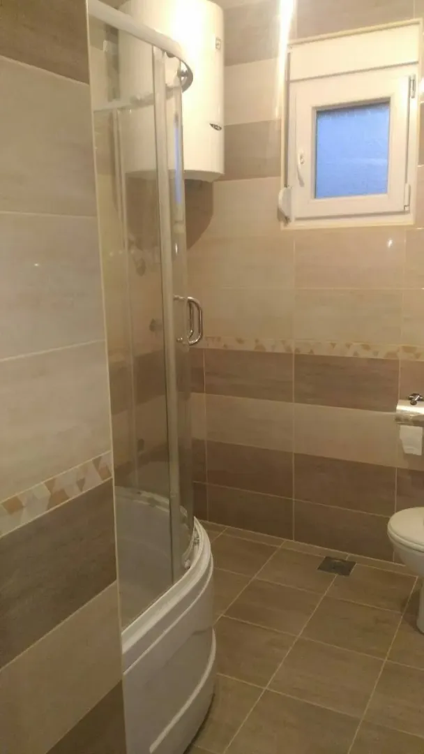 A simple bathroom with a shower cabin, boiler, and light tiles.