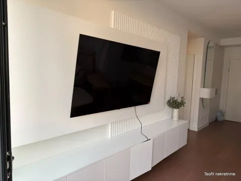 Dnevna soba sa modernom zidnom oblogom, televizorom i belim elementima. - image 6