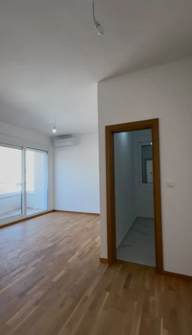 Prazna soba sa parketom i vratima koja vode u hodnik.