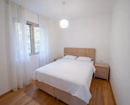 Bedroom with a double bed, bedside tables, and a window with white curtains. - image 6