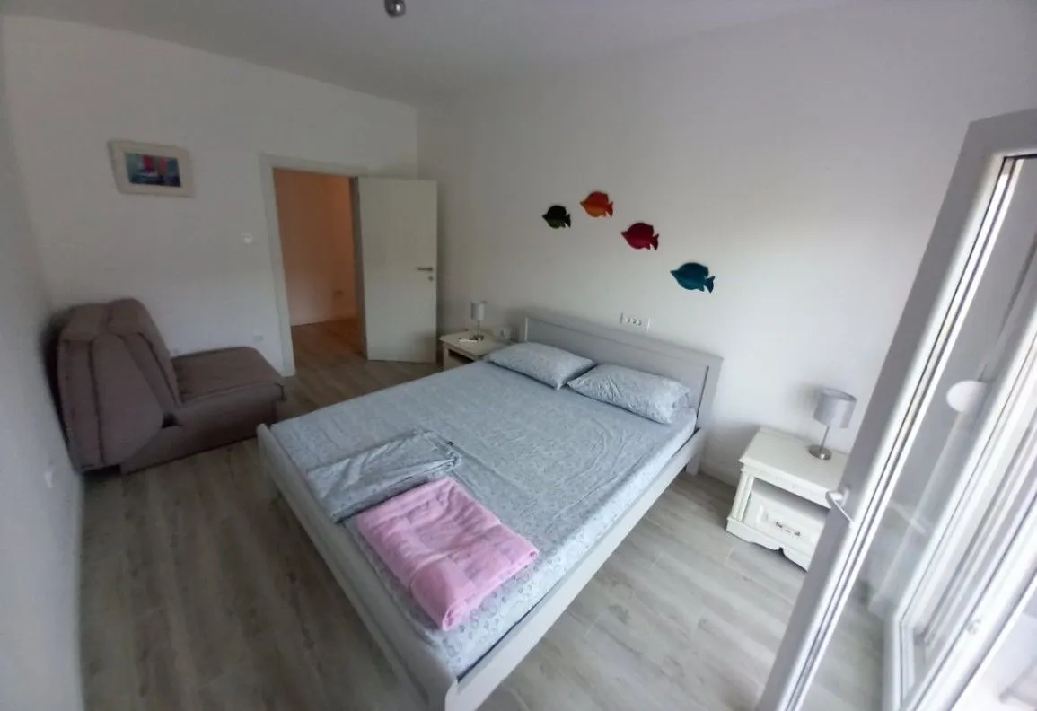 Svijetla spavaća soba sa bračnim krevetom, noćnim stočićima i foteljom.