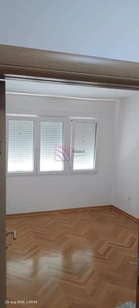 Empty room with hardwood flooring and windows.