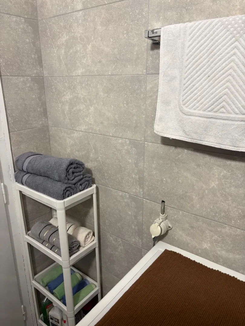 A corner of a bathroom with grey tiles and a towel shelf.