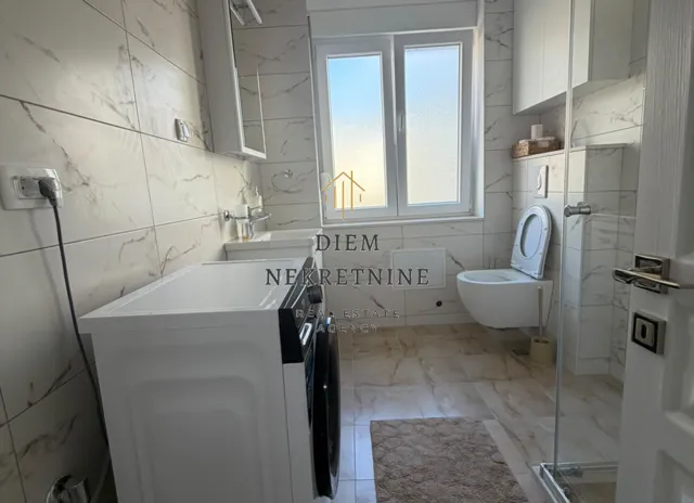 Modern bathroom with a washing machine, toilet, and walk-in shower.