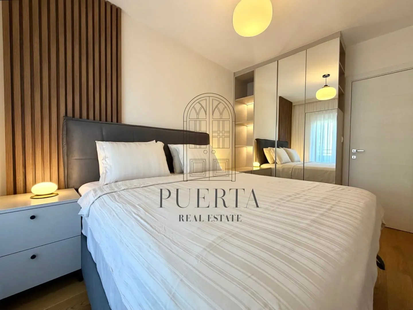 Modern bedroom with a double bed, wooden wall panels, and a mirrored built-in wardrobe.