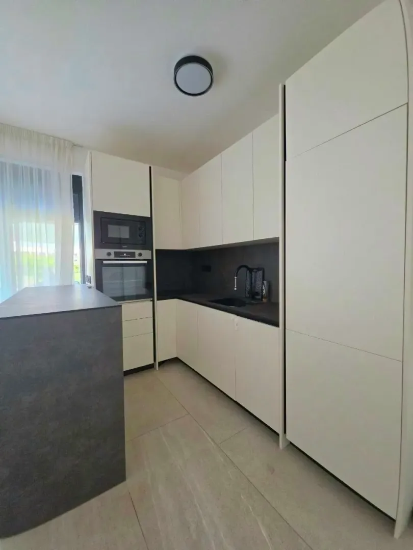 Moderna kuhinja sa bijelim elementima i tamnom radnom površinom.