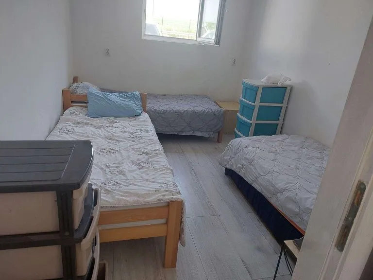 Spavaća soba sa više kreveta i plastičnim komodama.