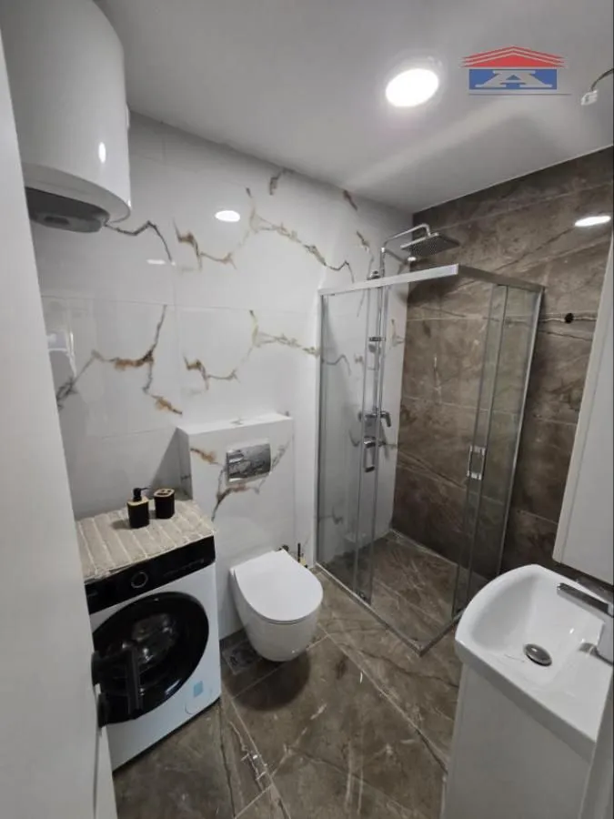 Moderno opremljeno kupatilo sa tuš kabinom, umivaonikom, veš mašinom i WC šoljom.