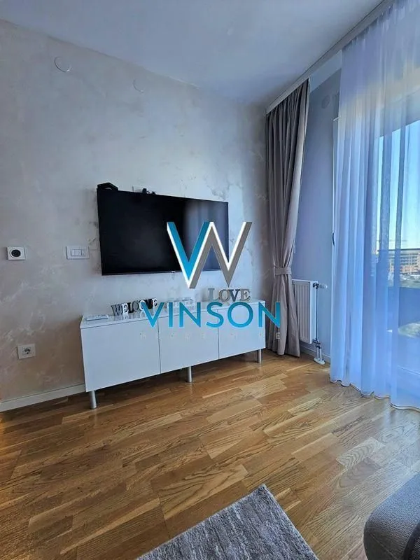 Dnevna soba sa TV-om, komodom i prozorom sa zavesama.