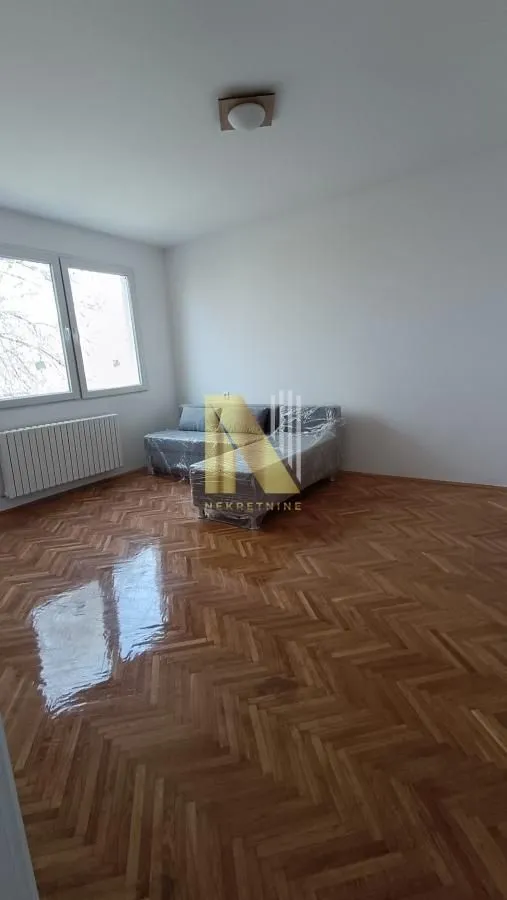 Prazna soba sa parketom i trosedom u foliji.