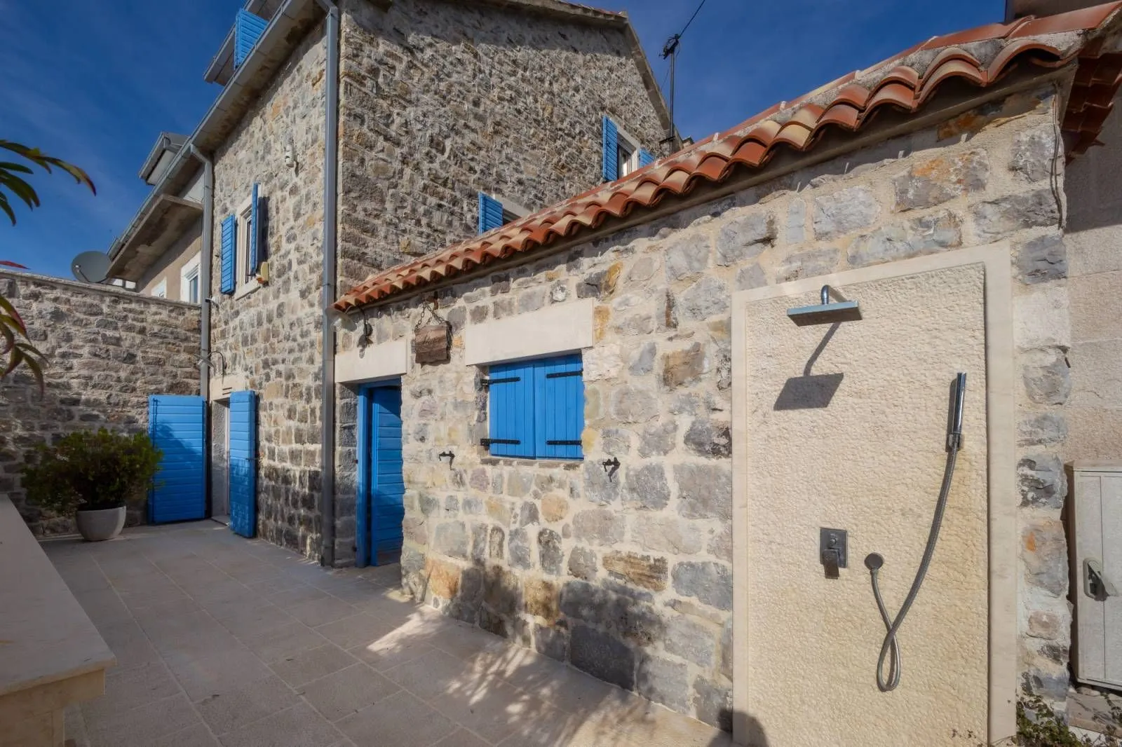 Courtyard of a traditional stone house with blue shutters and an outdoor shower.