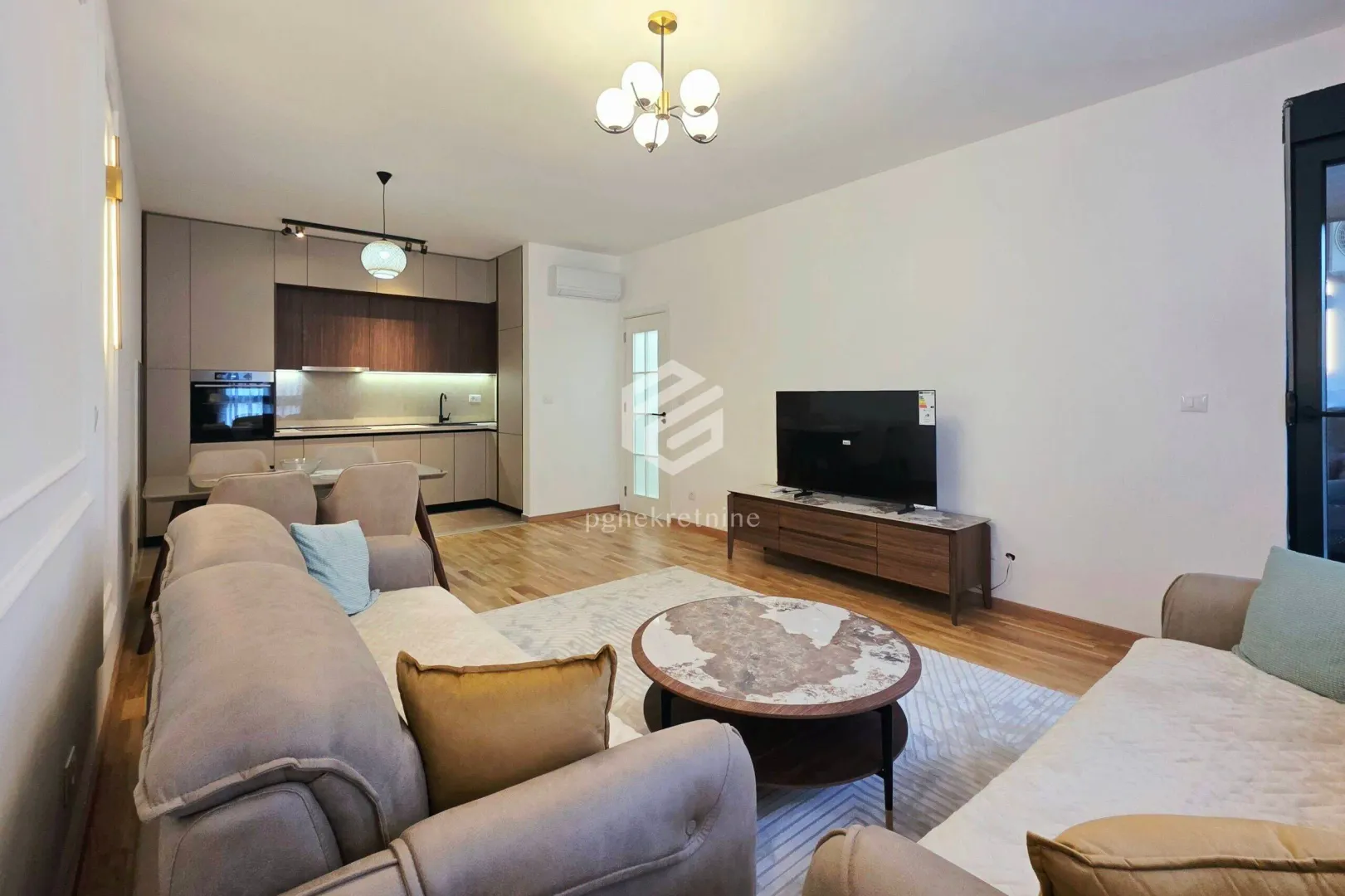 Spacious living room with a sofa set, TV, and kitchen in the background.