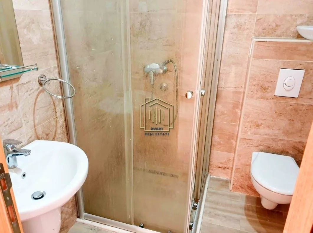 Kupatilo sa tuš kabinom, umivaonikom i ugradnom wc šoljom obloženo keramičkim pločicama.