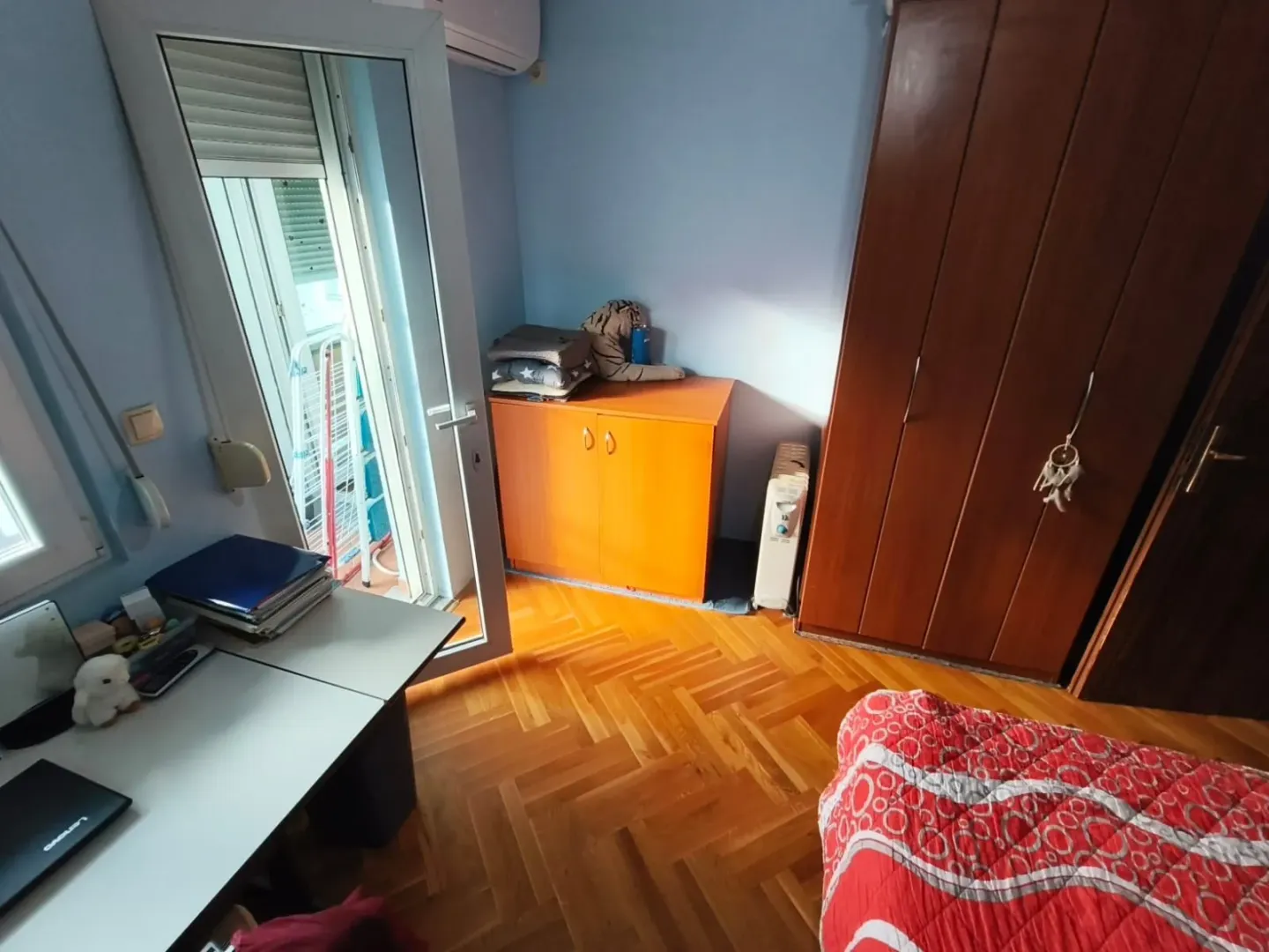 Manja spavaća soba sa krevetom, ormarom, pisaćim stolom i izlazom na terasu.