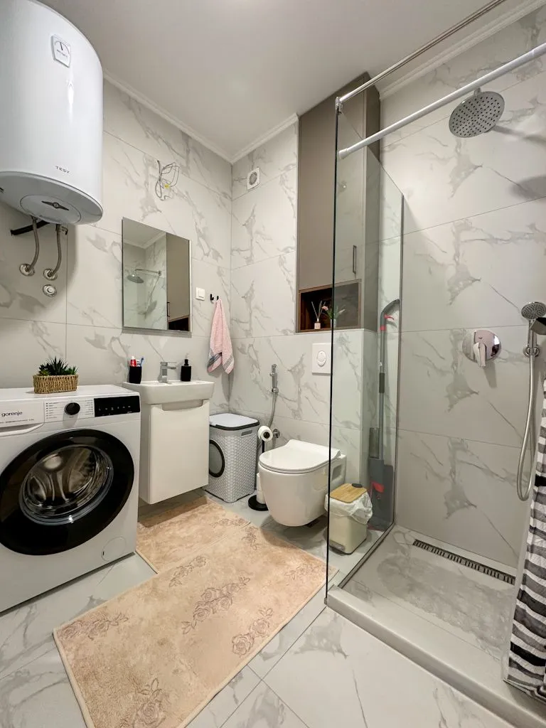 Modern bathroom with a walk-in shower, washbasin, and washing machine.
