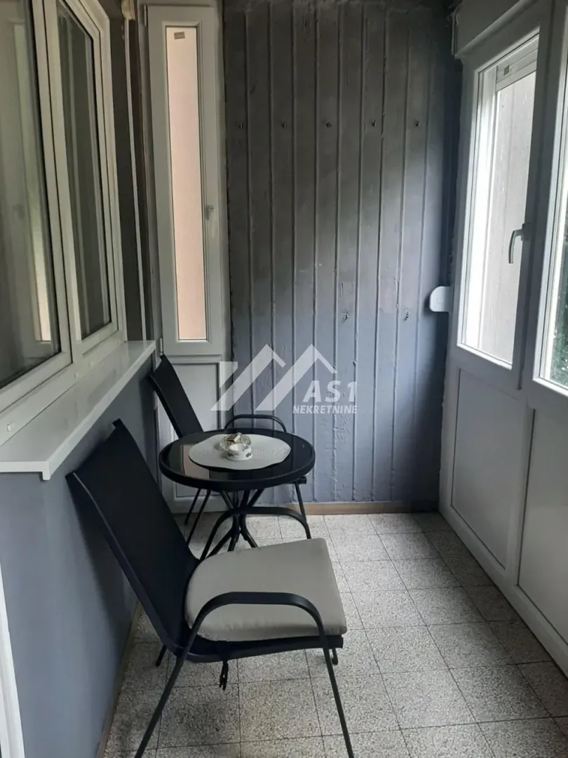 Zastakljeni balkon sa malim stolom i dve stolice.