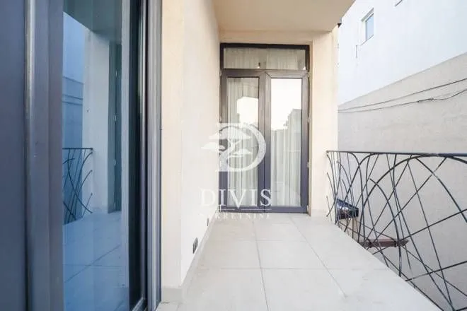 Natkriveni balkon sa popločanim podom i metalnom ogradom.