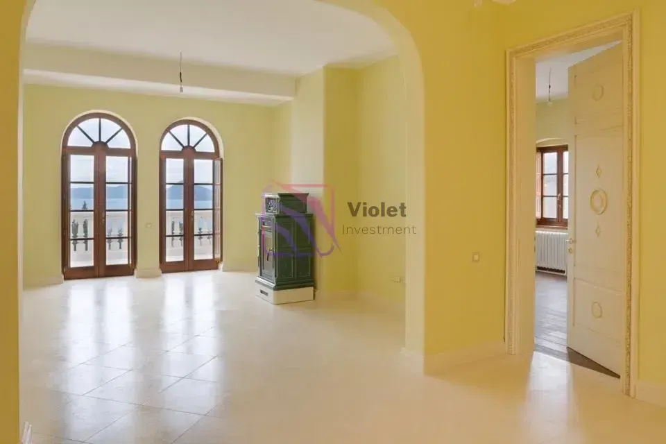 Prostrana prazna dnevna soba sa žutim zidovima, kamenim podom i balkonskim vratima.