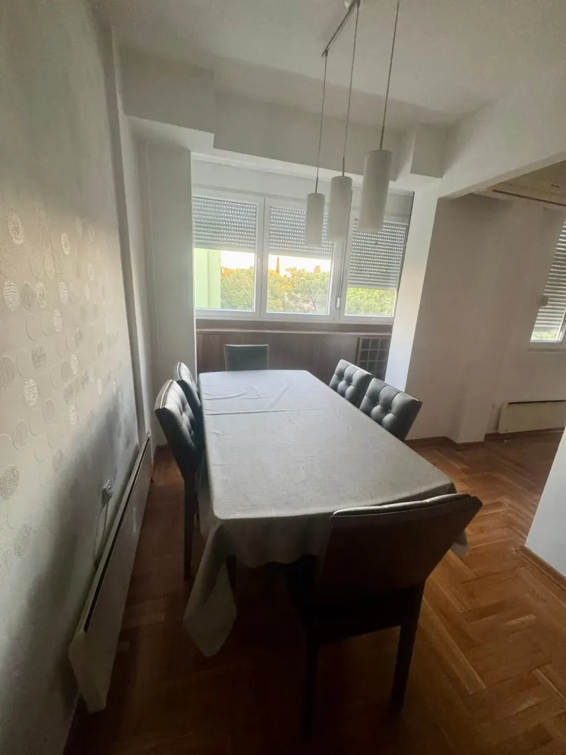 Trpezarija sa velikim stolom i stolicama pored prozora.