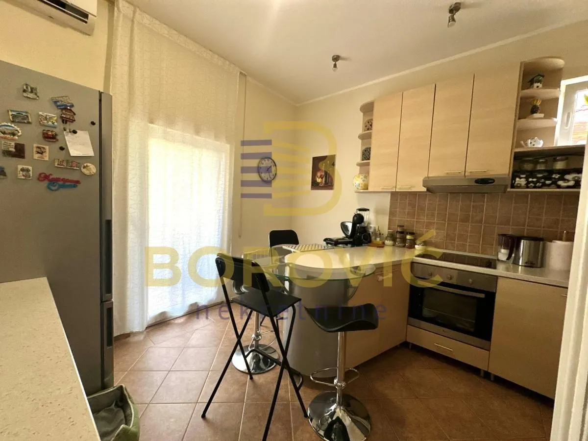 Kuhinja opremljena drvenim elementima i šankom sa barskim stolicama.