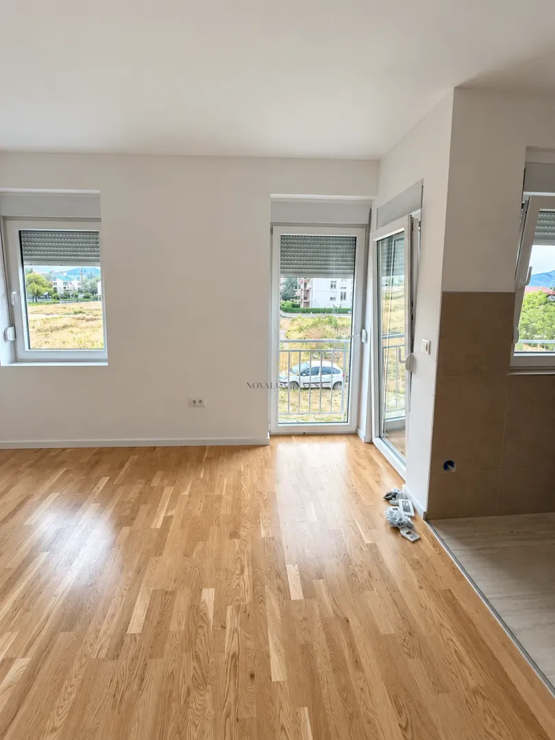Empty room with wooden flooring, white walls and access to the terrace.