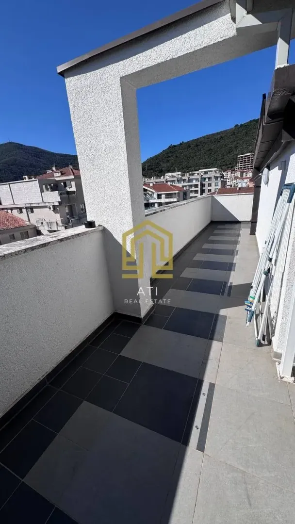 Prostrana popločana terasa sa pogledom na naselje i brda.