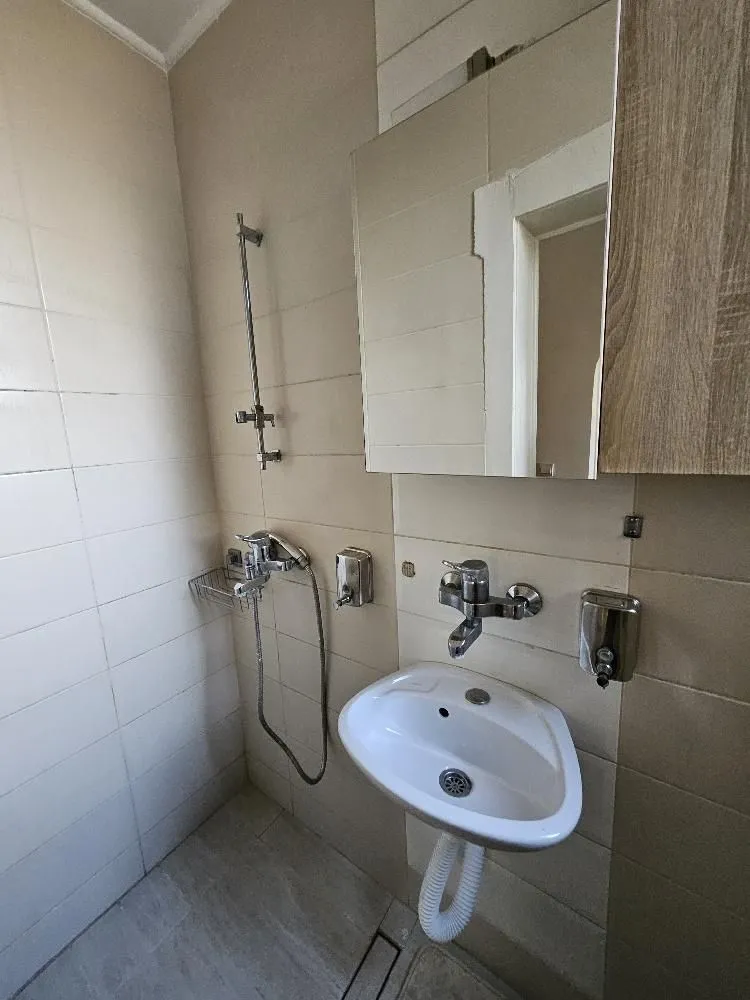 Manje kupatilo sa tuš kabinom, umivaonikom i ogledalom sa ormarićem.