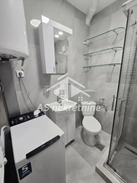 Modern bathroom with a shower cabin, washbasin, and washing machine.