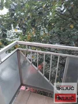 Manji balkon sa metalnom ogradom i pogledom na krošnje drveća. - image 9