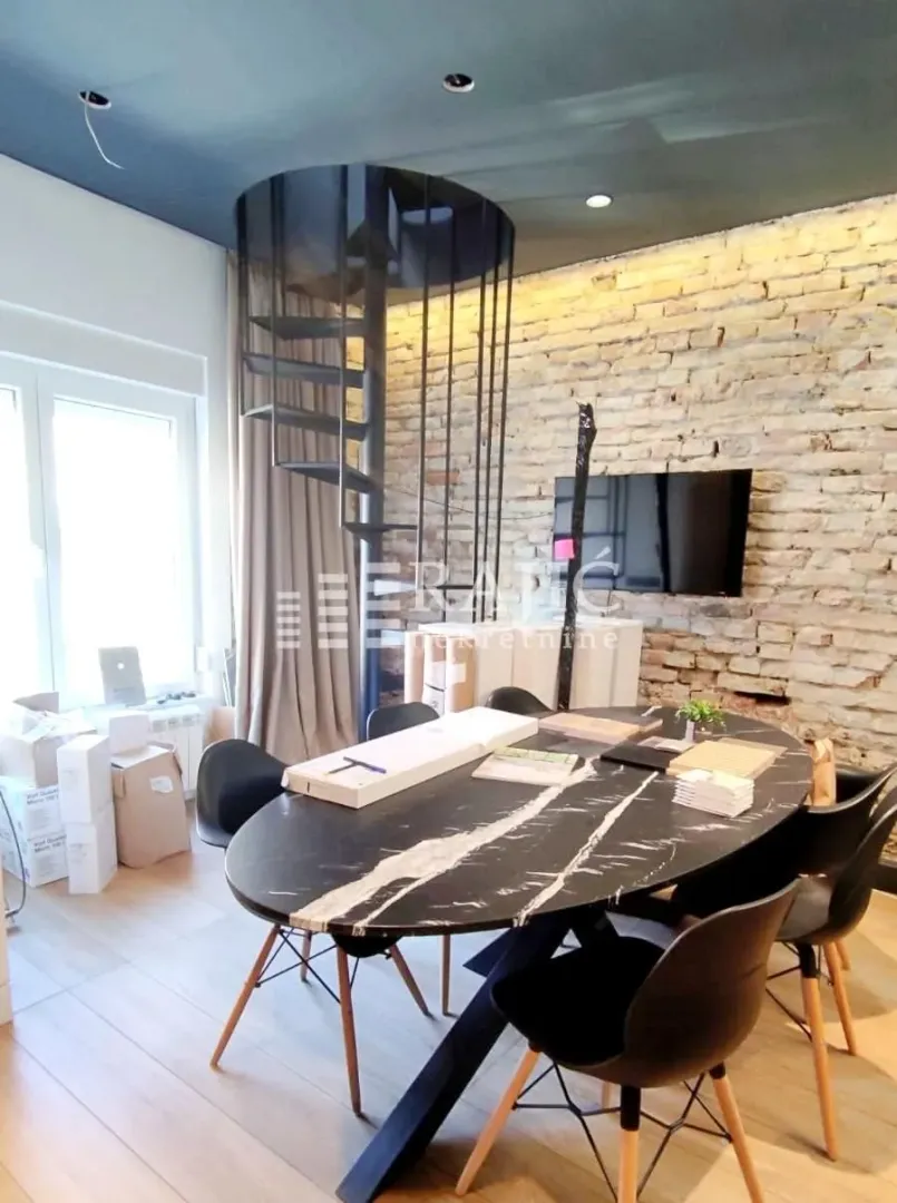 Living room with a dining table, spiral staircase, and exposed brick wall.