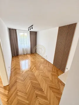 Prazna dnevna soba sa drvenim parketom, prozorom i dekorativnim drvenim panelom na zidu. - image 3
