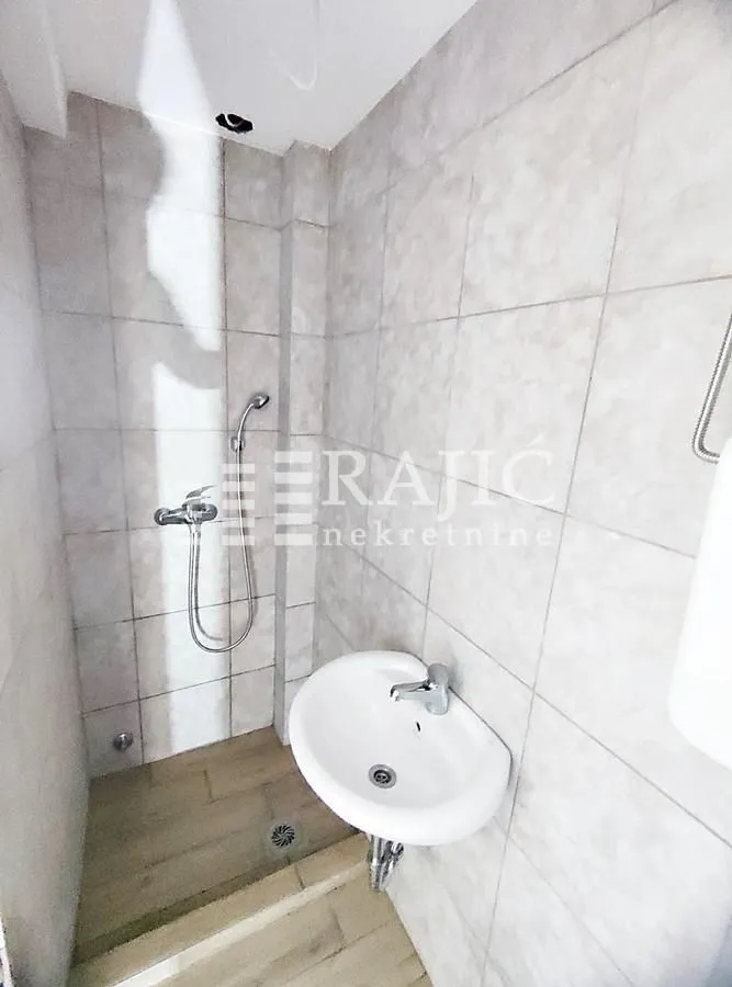 Smaller bathroom tiled with ceramic tiles featuring a sink and a shower.